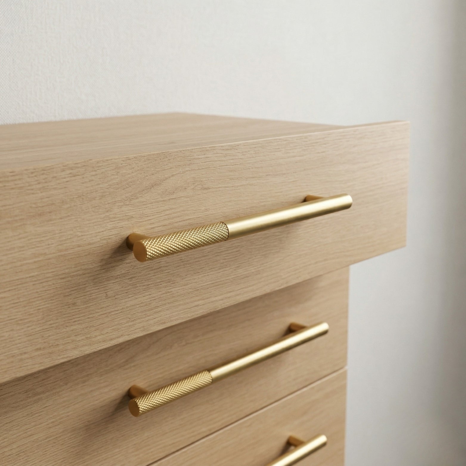 Premium antique brass and PVD gold knurled drawer handle installed on light oak wood furniture, featuring a textured grip and sleek professional finish.