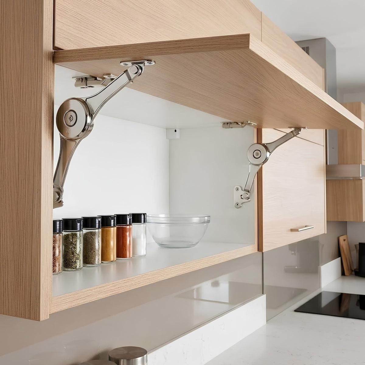Two Ebco Heavy Cabinet Stays installed in a modern overhead kitchen cabinet, holding a wooden shutter open above a shelf of spice jars