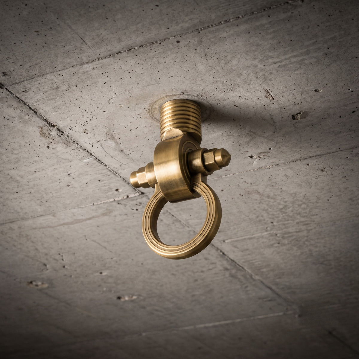 A modern, geometric brass-finished ceiling bracket for an indoor jhula (swing), seen in a detailed close-up and mounted securely on a raw concrete slab ceiling