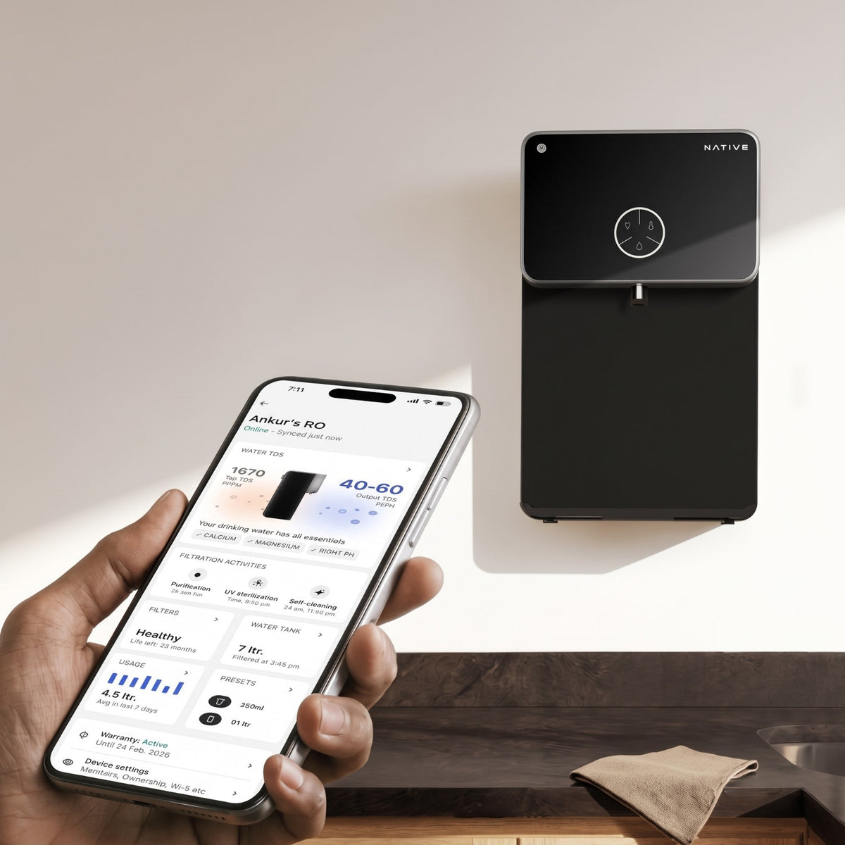 A person holding a smartphone to display the Native companion app, which shows water TDS levels and filter life, positioned in front of the wall-mounted purifier.