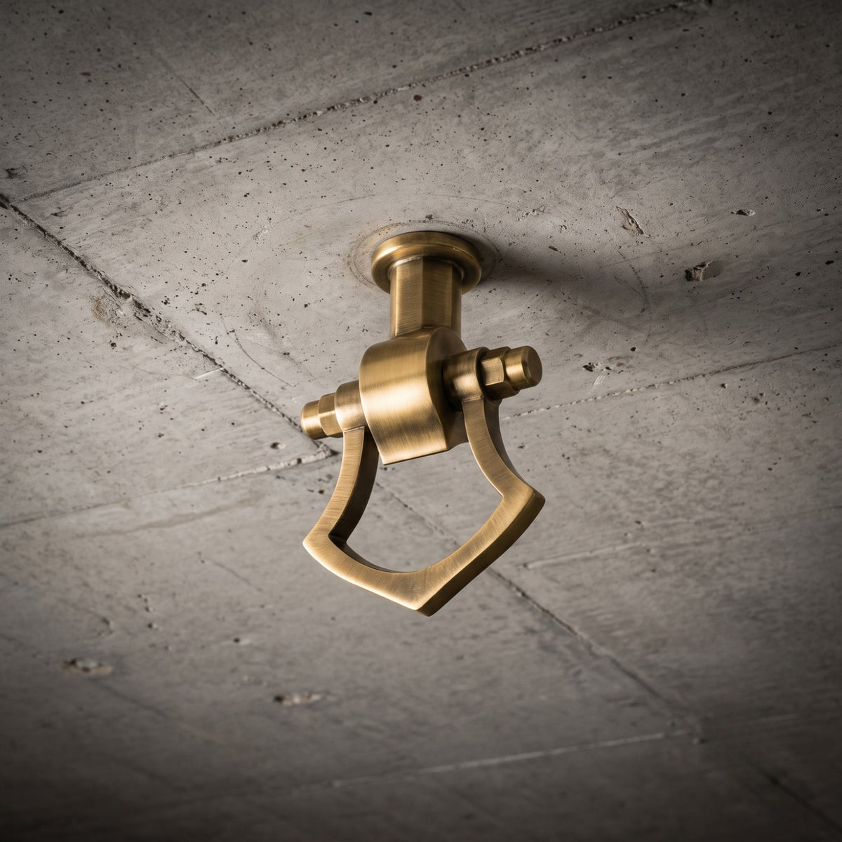 A traditional, heavy-duty brass-colored ring bolt style ceiling bracket (jhula kada) for an indoor or Indian swing, mounted in a raw concrete slab ceiling